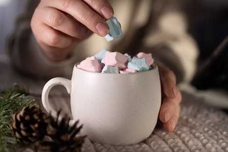 closeup hand placing pastel marshmallow, home barista arranging garnish on cocoa, pinecone and...