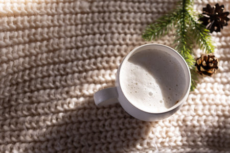overhead mug with creamy foam texture on knitted blanket. minimalist hygge scene with soft sunlight, neutralの写真素材