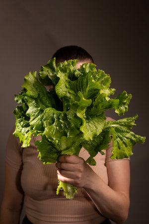 A woman stands in a studio holding a large head of vibrant green lettuce. The lettuce completely...