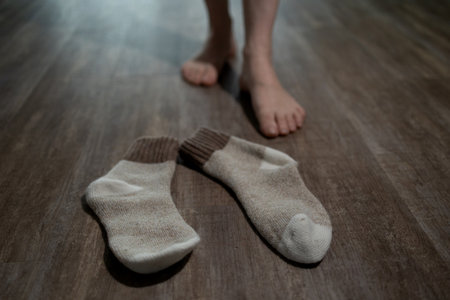 Bare feet approach a pair of socks on a wooden floor, suggesting the person has been enjoying the warmth from underfloor heating in a cozy home environment.の写真素材