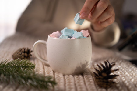 hand placing pastel marshmallow into ceramic mug on blanket, stylist arranging seasonal product shotの写真素材