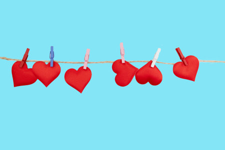 Small red hearts are clipped to a string with colorful clips. The scene features a bright blue background, making it suitable for Valentines Day designs and digital content.の写真素材