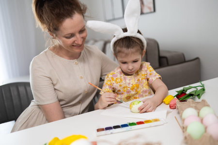 A happy mother and daughter sit together at a table, preparing for Easter.