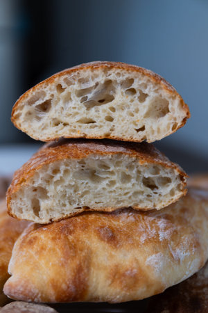 Loaves of bread are cut in half to show the soft inside and crispy outer layer. They sit on a wooden...
