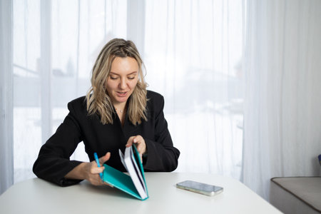 A business woman is seated at a table, holding a diary and a pen. She is focused on writing as snow...