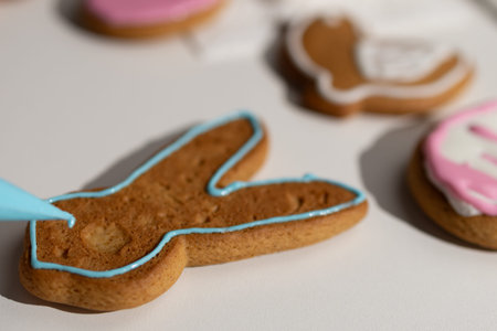 A gingerbread Easter bunny cookie is meticulously outlined with vibrant blue icing using a piping...