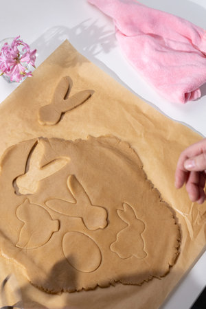A person bakes festive Easter gingerbread cookies, cutting bunny and egg shapes from light brown...