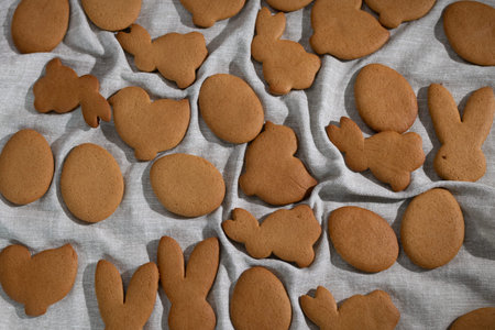 Gingerbread cookies are laid out on a cloth. The cookies are shaped like bunnies, eggs, and chicks....