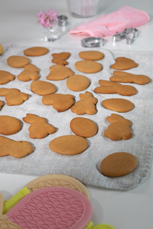 Numerous freshly baked Easter bunny and egg shaped cookies are arranged on a light linen cloth in a...