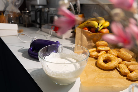 Homemade custard batter in glass bowl next to freshly baked ring pastries on kitchen counter. Sweet...