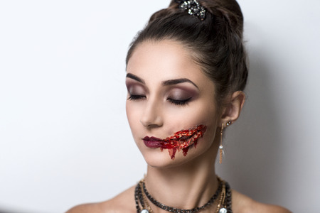 Female vampire with blood stains stage blood. Pretty woman with perfect face, smoky eyes, bright red lips sexy mouth, professional art make up. Evil crime murderer, offence furious lady, be a victimの写真素材