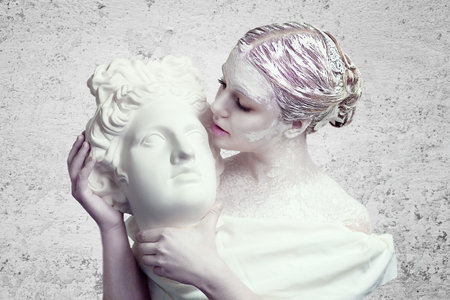 White pretty girl holding a porcelain marble head of a statue ancient warrior. Make up idea, body...
