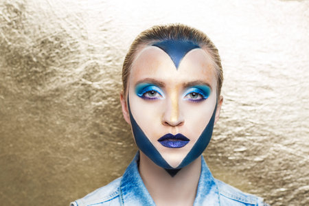 Beautiful magical charming woman love princess with big painted heart on face. golden hair. Figure paint on her cheek blush, bright shadows eye makeup glossy shiny lipstick lips, blue gold creativityの写真素材
