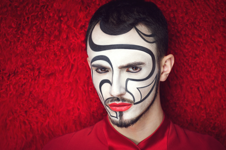 Creative make-up, new conceptual idea for Halloween. red black white bold body art painting. Crazy graphic abstract picture lines, handsome man face. curly fur background Horizontal professional photoの写真素材