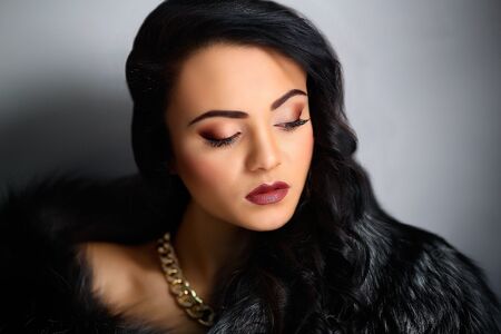 Beautiful young woman in a black fur coat and jewelry. Perfect Life of Reach Person. Dreams. Desire. Beautiful girl, professional photo, portrait. Bright model, make-up, jewelry. This photo is perfect for shops dealing with fur, accessory, jewellery. Can be used for poster, card, blog or magazine. Hand, fingers, nails. New year magic.の写真素材
