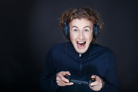 Guy playing games on the console, big headphones earphones. Press the buttons and control his virtual character. Team competition, gambling mania, idea computer addiction social problem in adolescentsの写真素材