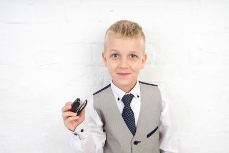 handsome blonde boy holding small stapler with staples in his hand. white wall studio, horizontal banner, professional photo. prepare for school, necessary office supplies. formal style business suitの写真素材