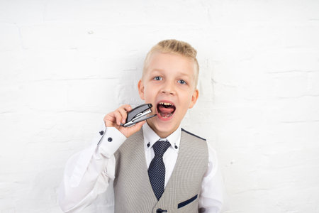 handsome blonde boy holding small stapler with staples in his hand. white wall studio, horizontal...
