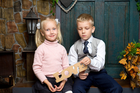 Little children hug and smile. Boy girl are holding in hands wooden sign word Love. Friendship affection, copying of adult behaviour social roles, small model of family. older brother younger sisterの写真素材