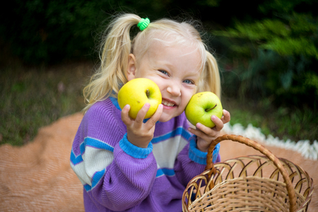 Funny little girl playing on nature on woolen blanket. Beautiful girlie holding yellow apple, relax in the garden. beauty of autumn park. Round shape of big apple. day picnic in the village, fresh airの写真素材