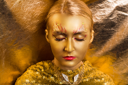 Creative makeup, new crazy conceptual idea for Halloween. golden red bold body art painting. Crazy new graphic abstract picture on woman face. shiny lipstick gloss lips Horizontal professional photoの写真素材
