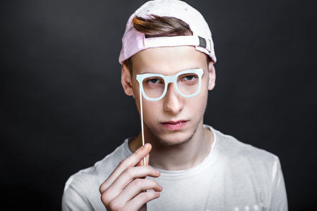 Paper eyeglasses hand made crafts, accessories cardboard attributes on sticks for a professional photo shoot. Young man holding vision in his arm. Expressing emotions of serious person love studyingの写真素材