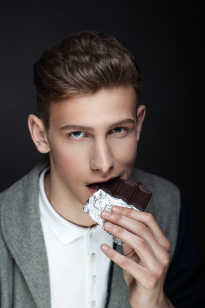 Stylish man close up portrait. Fashion jacket sexy bad boy. Black guy with fashionable haircut. Vertical banner conceptual idea about unhealthy food, eating chocolate candies the effects of toothacheの写真素材