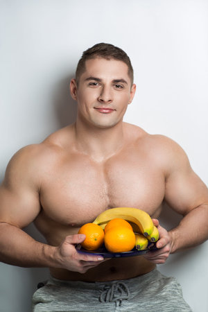Strong pumped man holding fresh fruit in hands. Pectoralis major, biceps, triceps sexy torso....