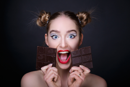 Beautiful woman, holding in her hands big chocolate bar. Two hums of hair. Professional cosmetics makeup. Red matte lipstick lip-gloss. New photo close up portrait, black color background horizontalの写真素材