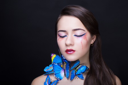 Bright blue butterflies seating on woman head, hair, neck. Oriental beauty girl professional makeup. Portrait of a beautiful lady who wore big accessory. Young fortune teller predicts fate horoscopeの写真素材