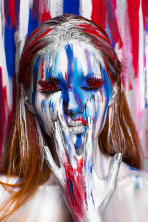 Girl painter holding lips with silver fingers, all body Painted in gouache watercolor acrylic oil paints. Creative makeup new conceptual idea. Crazy new graphic abstract picture wall, woman face linesの写真素材