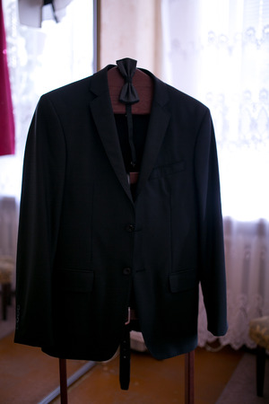 Black stylish jacket weighs on a hanger, a small bow tie is tied. Suit for a groom wedding or an official event. new cut and style of men's fashion. Beautiful fabric and quality seams. clothing storeの写真素材