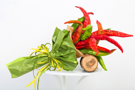 Red and green hot pepper wrapped in wrapping paper, vegetables are collected in a bouquet on white background.の写真素材