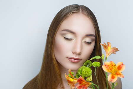 Beautiful woman with orange flowers, long clean combed hair, necked shoulders. Professional cosmetics nude makeup. Beige shiny lipstick. New photo close up portrait, gray color background horizontalの写真素材