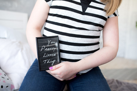 Pregnant woman holding black card with white inscription you pretty little thing. Creative accessory bright idea part of body, horizontal lines striped T-shirt. Professional closeup photo new art ideaの写真素材