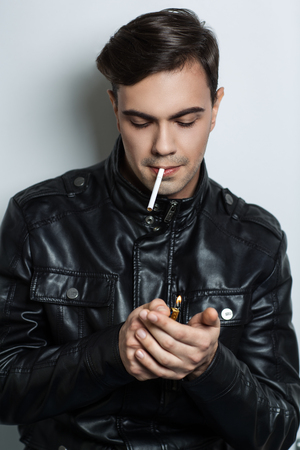 Stylish man clutched a cigarette in his mouth. Keep a lighter in his hand and going for a smoke. Leather jacket sexy bad boy. Black guy with fashion haircut. Vertical banner, conceptual idea smokingの写真素材