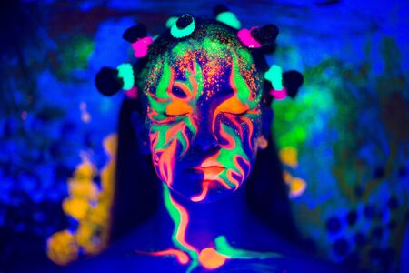 Creative woman lady girl model shine with blue green orange colors. New Bright conceptual art make-up glows under ultraviolet light. Club disco neon party time. Drink alcohol feel wild energy of musicの写真素材