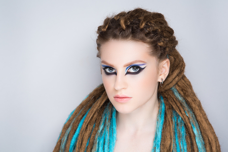 Young beautiful girl woman with brown, blue dreadlocks. Stylish volume hair-do, professional make-up art creative, liner shadows new cosmetics. Bright colorful makeup, massive hair. Afro weave braidsの写真素材