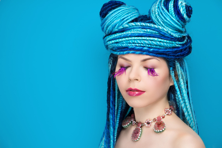 Girl woman creative make-up. Massive necklace jewelry. Shadows painted on her face. Purple crimson lips, eyes liner. Hair dreadlocks braided, blue strings. Head wound with dreads, horns twisted hairの写真素材