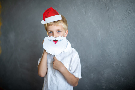Prepare for the new year party, funny Santa Claus. Beautiful handsome boy with a cardboard eye glasses. Blonde holding a decoration on a wooden stick. Original accessories for photo shootsの写真素材