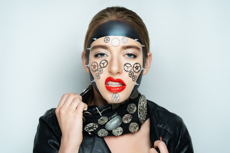 Portrait of a beautiful steampunk woman over gray background. Vintage accessory black metal clock necklace. Massive silver accessory. Creative art make up. gears, mechanical parts bolts. Mask make-upの写真素材