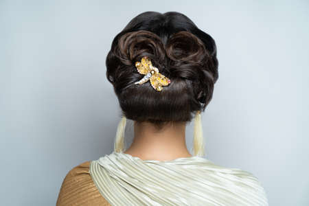 Close-up portrait of beautiful girl with volume hair-do. Luxury hair styling. Woman with gathered medium length hair. Wedding hairstyle decorated by accessory. Beauty bride style, creative jewelry pinの写真素材