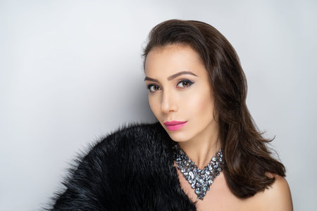 Beautiful girl puts on a gorgeous fur coat made of expensive mink fur. Luxury jewelery decorates her neck, exclusive necklace made of gem stones. Perfect horizontal banner for new clothes storeの写真素材