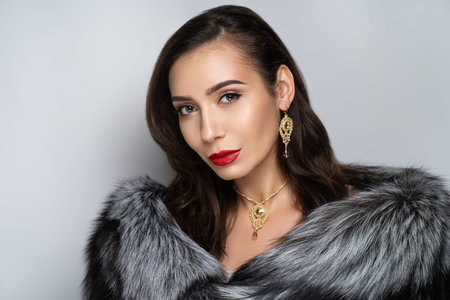 Beautiful girl puts on a gorgeous fur coat made of expensive silver fox fur. Luxury jewelery...