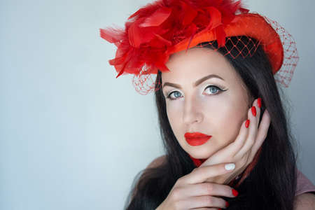 Beautiful woman skincare concept. Bright makeup with arrows shades shadows sequins. Evening hairstyle brunette long straight hair. background horizontal gray banner. New big red hat, massive feathersの写真素材