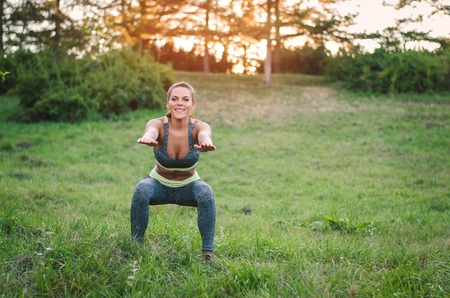 Attractive fitness woman practicing in the park on the grass. She is doing squat exercise.の写真素材