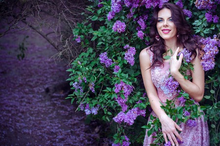 beautiful girl with dark hair in a pink dress standing in the garden lilac bushesの写真素材