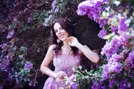 beautiful girl with dark hair in a pink dress standing in the garden lilac bushesの写真素材
