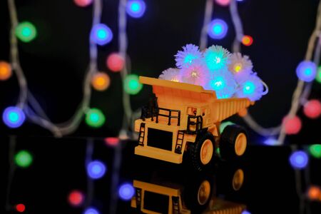 Christmas card. Happy Chrismas Concept. Children's yellow car carries bright festive garlands. Dark background, yellow color.の写真素材
