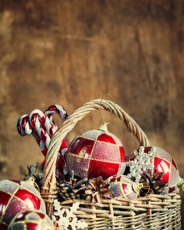 Christmas Composition with Vintage Country Gifts on Warn Wooden Background. Basket, red balls, pine cones, sweets. Copy spaceの写真素材
